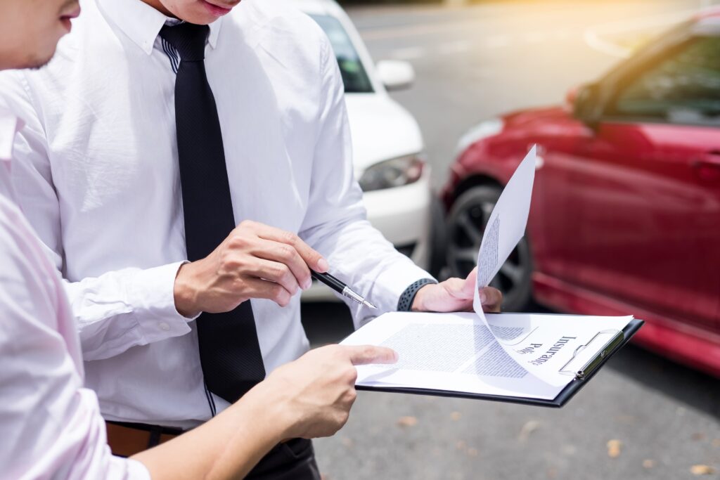 Insurance representative assessing and processing a car accident claim standing next to the damaged cars