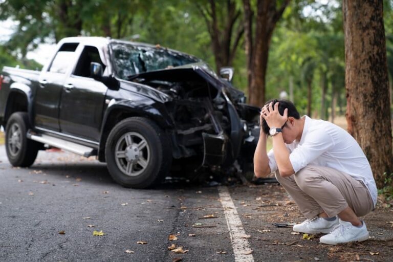 A car accident victim man is holding his head and waiting for insurance call center on the road.