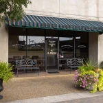 Front view of McCutcheon & Hamner's office, with a sign, benches, plants, and a green-striped awning in Athens, Alabama.