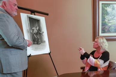 Attorney joel hamner explains an elevator accident exhibit to a client, showing maintenance log evidence.