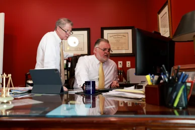 Tom mccutcheon and joel hamner talk with a client in joel’s office about pursuing compensation for serious back injuries.