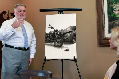 Attorney Joel Hamner discusses a wrongful death case with a family member, showing a drawing of a motorcycle and car.