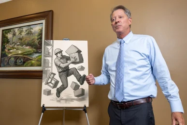 Attorney Tom McCutcheon discusses an Athens, Alabama personal injury case, standing beside an illustration of a construction.