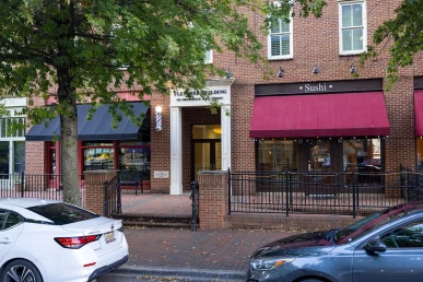 Fletcher Building is nestled between a barber shop and sushi restaurant, with trees and parked cars nearby.