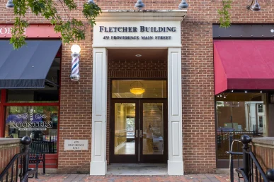 Fletcher Building's front doors view, showcasing brick facade and nearby Roosters Men's Grooming Center in Providence.