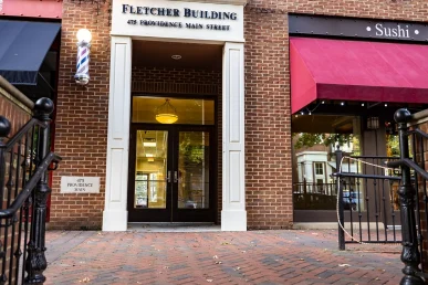 Front entrance of Fletcher Building at 475 Providence Main Street, with a barber pole and nearby Sushi restaurant awning.