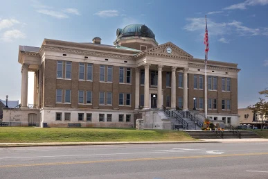Limestone County Courthouse features a grand façade with pillars, a clock, and a dome, set against a clear blue sky.