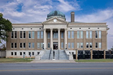 Limestone County Courthouse front with stairs and a statue centered at the base under a blue sky.
