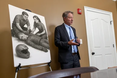 Tom McCutcheon discusses a traumatic brain injury case with a client, beside an illustration of paramedics assisting an.