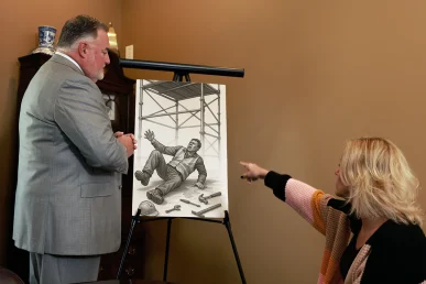 Joel Hamner discusses a workplace injury case, pointing at an illustration of a worker falling, with tools scattered around.